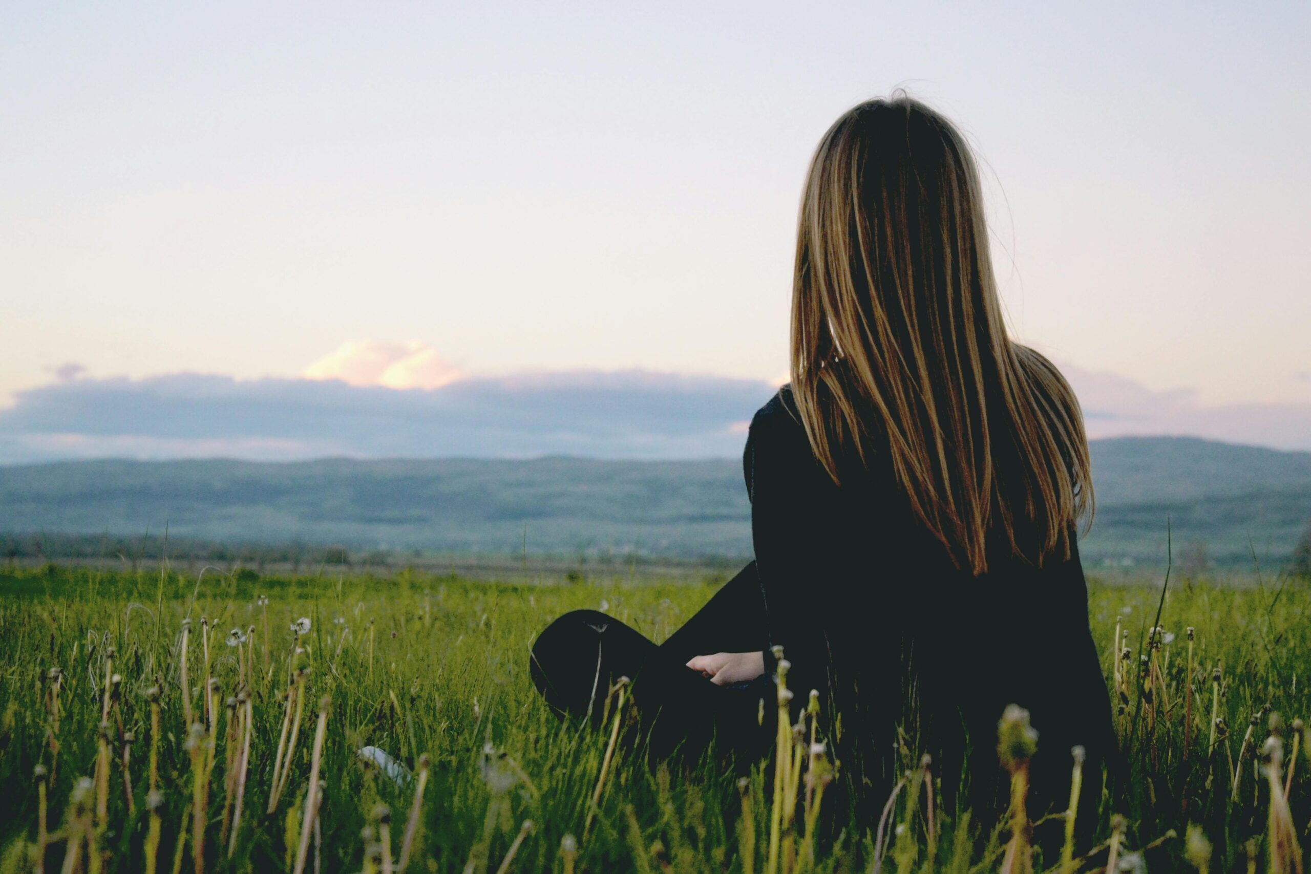 Woman enjoying peace in a lush green field with a scenic mountain view during sunset.